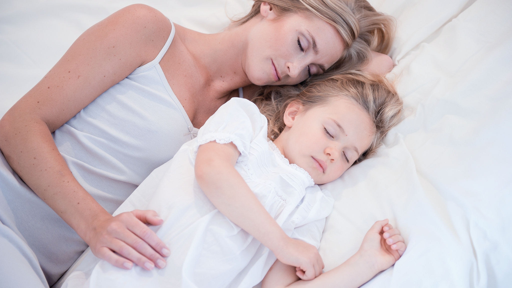 Mama i ćerkica spavaju jedna pored druge u belom krevetu na čistom vazduhu
